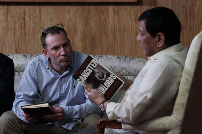 PICKING ONE’S THOUGHTS. President Rodrigo Roa Duterte, holding the book 'Gangster Warlords', talks to the book's author himself Ioan Grillo in Malacañang on Tuesday night. KING RODRIGUEZ/Presidential Photo