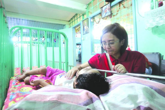 Comforting presence.  Edge Davao reporter Tiziana Celine Piatos tries her hand at comforting a weeping physically challenged child by gently rubbing her during the annual joint outreach program of sister companies Edge Davao and Zion Accuprint Publishing, Inc. in partnership with McDonald’s at Missionaries of Charity Home of Love in Juna Subdivision, Davao City yesterday.  LEAN DAVAL  JR.