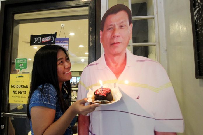 CREATIVE GESTURE. City Information Office staff Funny Pearl Gajunera has her photo taken beside a standee of President Duterte while holding a miniature birthday cake for the president at a local restaurant on Tuesday. President Duterte quiet celebrated his birthday with family and friends in the city. LEAN DAVAL JR.