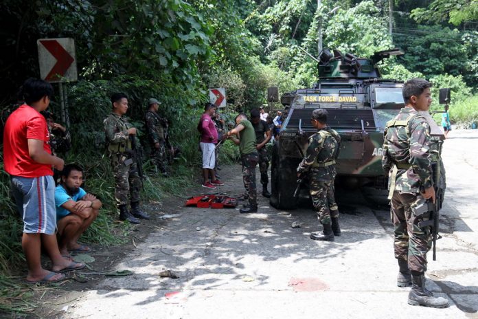 NOT EXEMPTED.Task Force Davao personnel stand guard while their comrades fix a light armor vehicle known as Simba which was hit by the New People’s Army’s Improvised Explosive Device (IED) during the rebel group’s attacked of Lapanday Box Plant in Mandug, Davao City on Saturday. LEAN DAVAL JR.