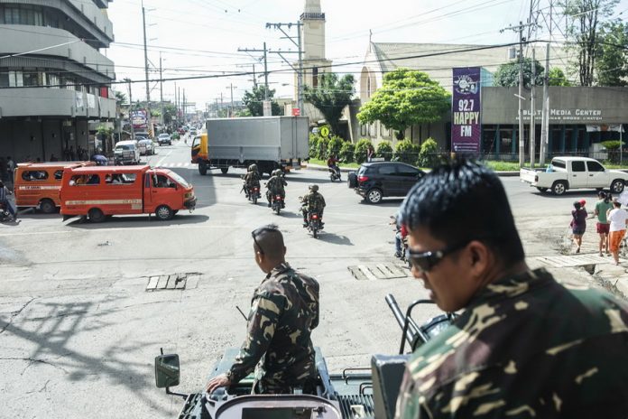 Army troops in an armored personnel carrier stand guard in one of the streets in downtown Cotabato City Wednesday (24 May 2017) as residents pass just like normal times. President Rodrigo Duterte declared martial law in Mindanao late evening Tuesday hours after members of the Maute Group terrorized Marawi City. MindaNews photo by Ferdinandh Cabrera