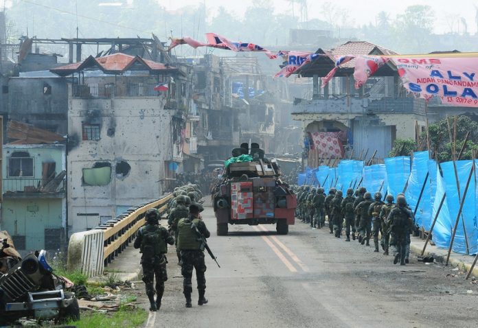 Damaged buildings loom in the background as Philippine Marines backed by a V300 armored vehicle cross Mapandi Bridge in Marawi City on Wednesday (Aug. 30, 2017), 100 days since the Islamic State-inspired Maute group started a siege that has made the city a ghost town. Government troops recaptured the bridge from the militants late last month. MindaNews photo by FROILAN GALLARDO Aug 30, 2017