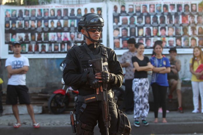 BATTLE-READY. A member of the Davao City Police Office Special Weapons and Tactics (SWAT) stands guard as part of the tightened security measures during the commemoration of last year’s September 2 Roxas Night Market bombing. The Maute terror group, whose members’ faces are printed on streamers in the background, was believed to be behind the attack that claimed 15 lives and injured 67 others. LEAN DAVAL JR.