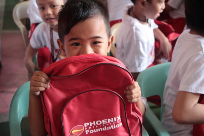 A kindergartener smiles behind his Phoenix Foundation backpack in a program where Phoenix employees spent time with the students and had games, food and performances.