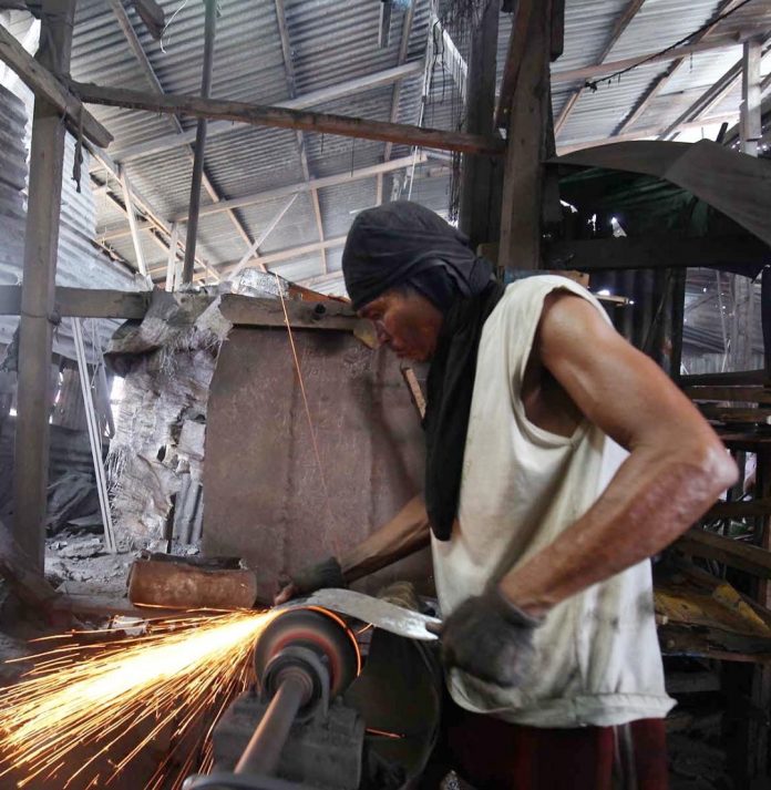 A blacksmith sharpens a newly-made long knife locally known as 