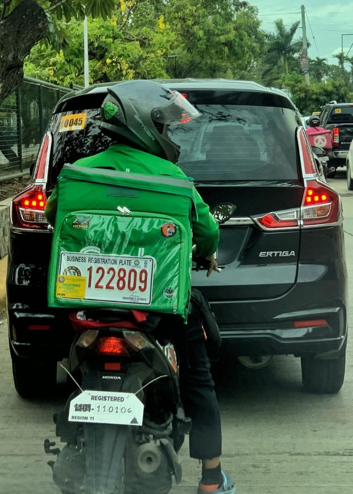 A delivery rider places his business registration plate on a thermal bag attached to his motorcycle in Davao City on Saturday. A group of food delivery riders submitted a petition to the City Council to stop requiring business permits for delivery riders in Davao City as a mandate by the city government. LEAN DAVAL JR.