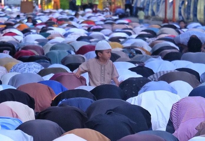 A young boy watches as devout Muslims perform sajda or prostrate during a congregational prayer to mark Eid'l Fitr, the end of the month-long Ramadan, along Roxas Avenue in Davao City on Wednesday morning. LEAN DAVAL JR